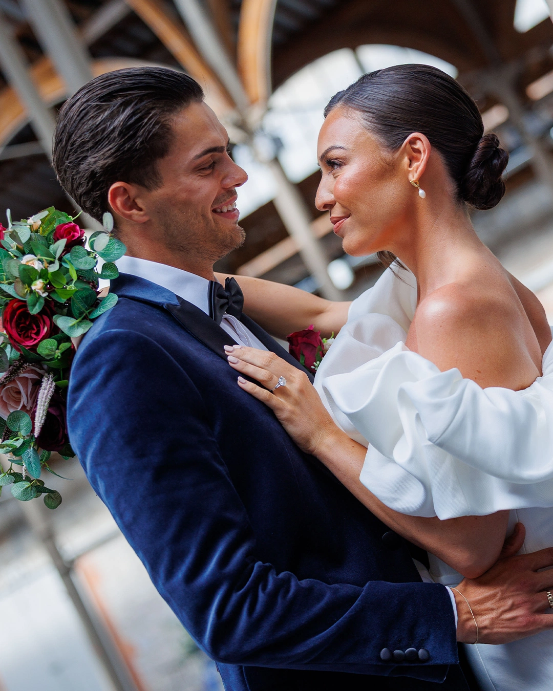 Happy bride and groom embracing on their wedding day, decorated venue backdrop.